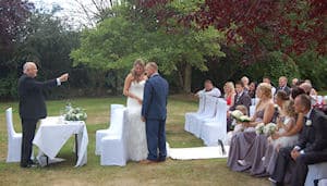 Peter York conducting an outdoor wedding ceremony for a couple with seated guests